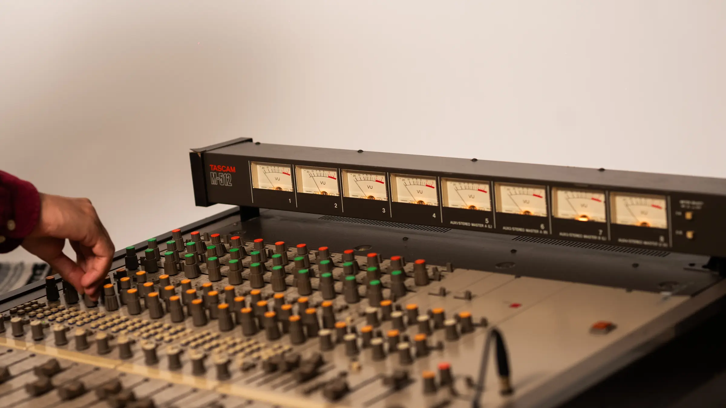 Hand adjusting the knobs of a Tascam M-512 console, its VU meters lit